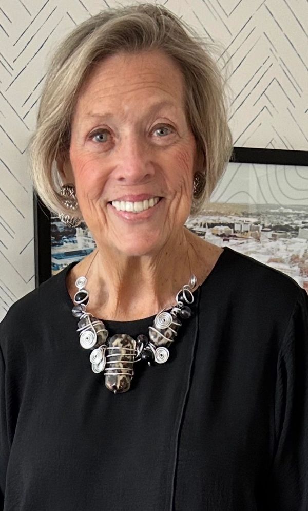 Smiling elderly woman with stylish necklace and black top.