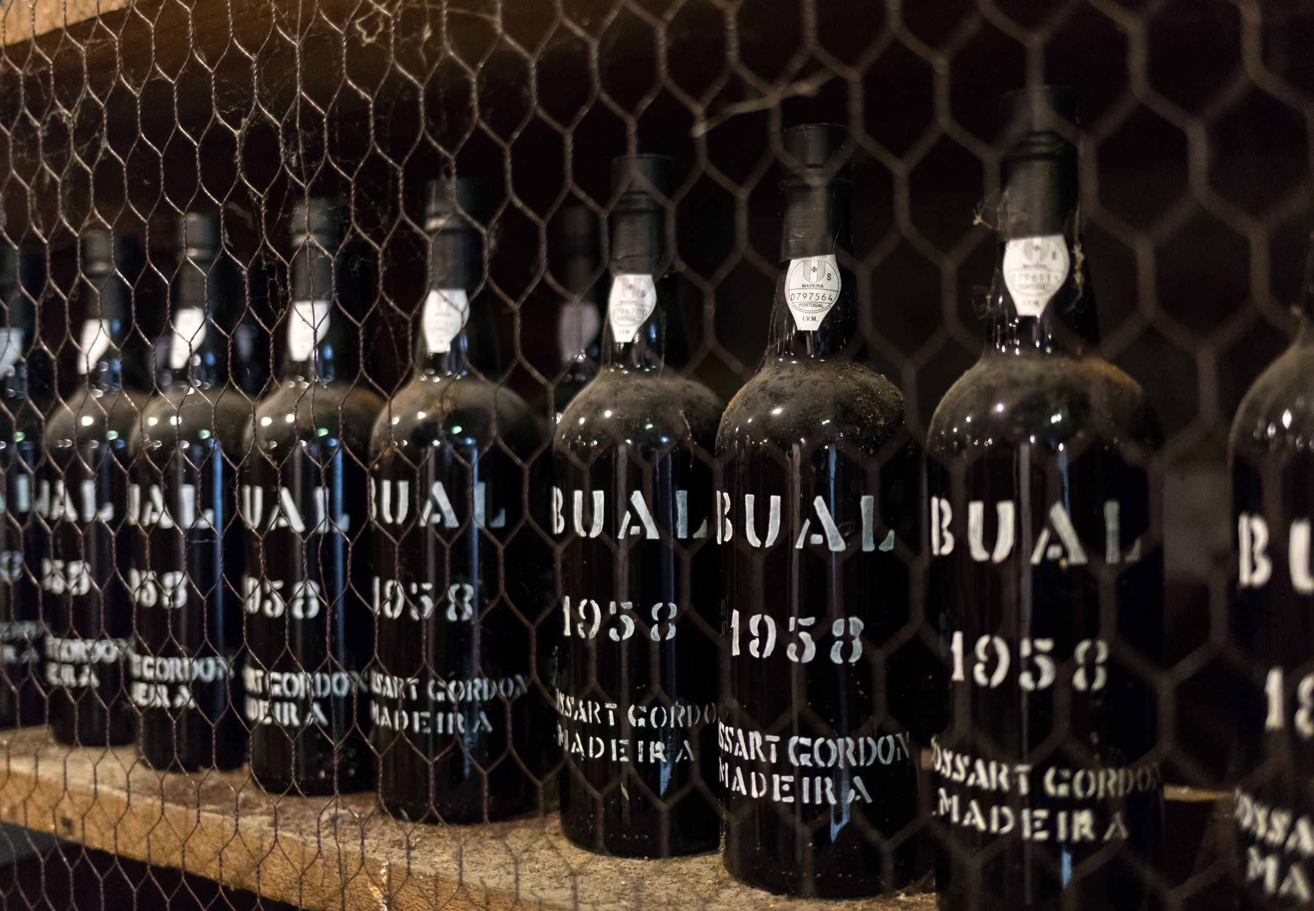 Vintage Bual Madeira wine bottles from 1958 behind wire mesh.