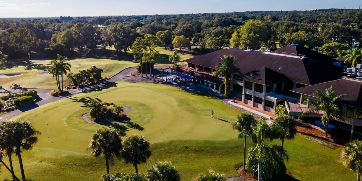 A golf course with a clubhouse surrounded by trees under a clear sky.