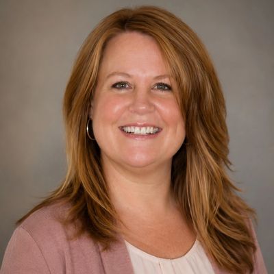 Smiling woman with light brown hair and a pink blazer.