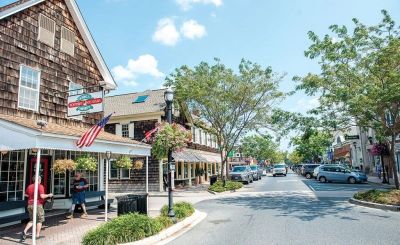 A sunny street scene in a small town with shops and trees.