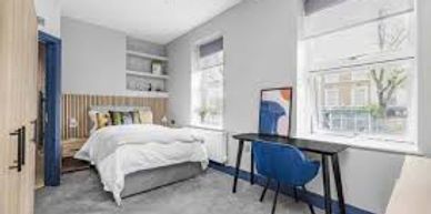 Modern bedroom with bed, desk, and large windows.