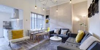 Modern living room with gray sofas, yellow accents, and an open kitchen.