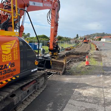 
An orange Hitachi excavator on a construction site next to a road.