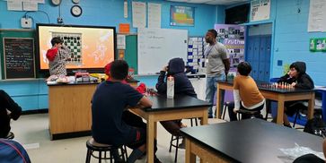 A classroom with students and a teacher discussing chess strategies.