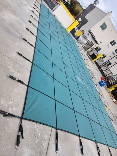 Large blue safety cover secured over an outdoor pool.