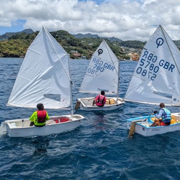 Three people sailing small boats on blue sea.