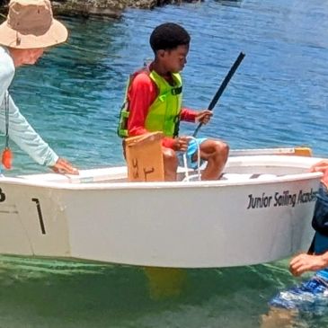 Boy in a boat with life jacket learning to sail.