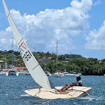 Person sailing a small sailboat under a partly cloudy sky.