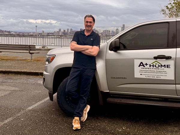 Man leaning on home inspection company truck in a cloudy urban setting.