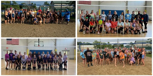 Large group photo of people on an outdoor sandy volleyball court.