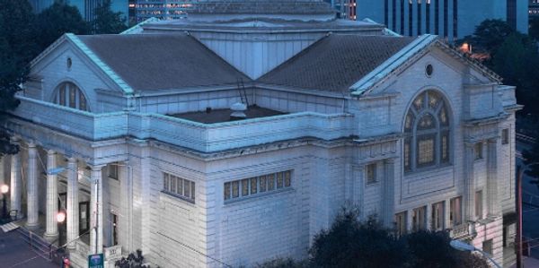 Historic neoclassical building with a dome, lit up at dusk in an urban setting.