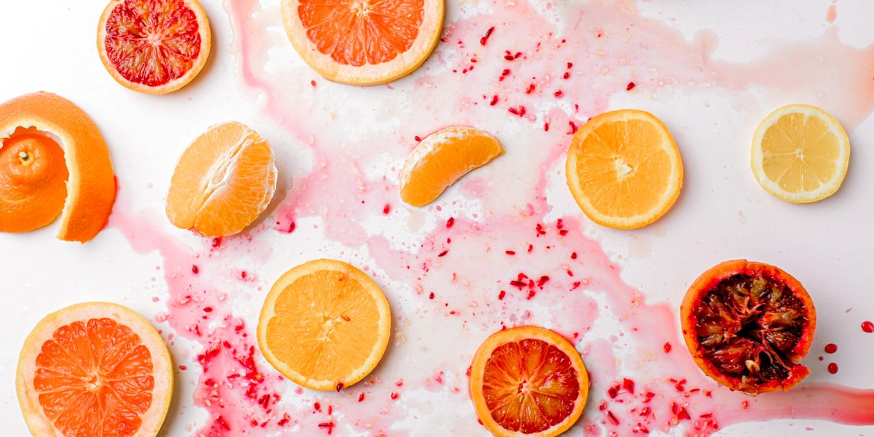 Slices of citrus fruits with juice splatters on a white surface.