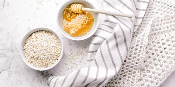 Bowls of oats and honey with honey dipper on a marble surface.