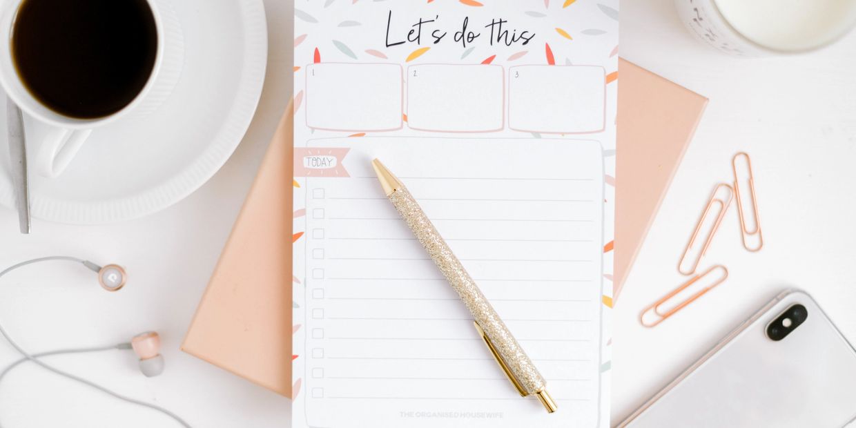 A cozy workspace with a coffee cup, glitter pen, planner, and earphones.