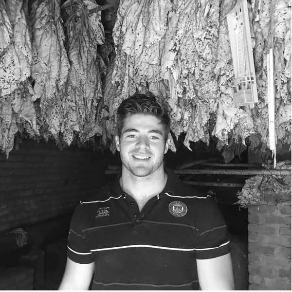 A young man smiling under hanging dried leaves in a rustic setting.