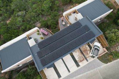 Aerial view of a modern building with solar panels on the roof surrounded by greenery.