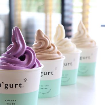 Four cups of colorful soft serve frozen yogurt lined up indoors.