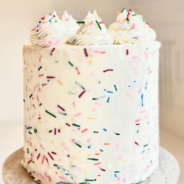 Tall white cake with colorful sprinkles and whipped cream dollops on top.