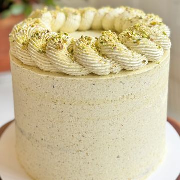 Tall pistachio cake with smooth frosting and piped topping.