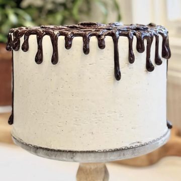 A smooth white frosted cake with chocolate drip decoration on top.