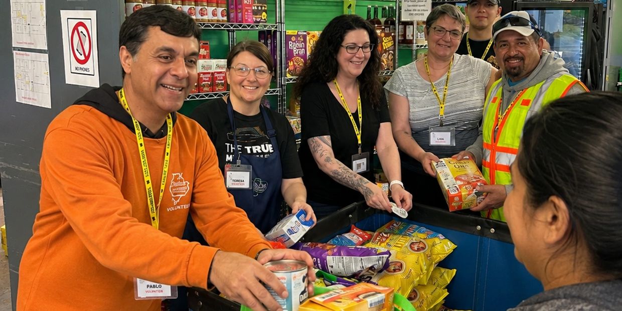 Volunteers happily distribute food items to a community member at a food pantry.