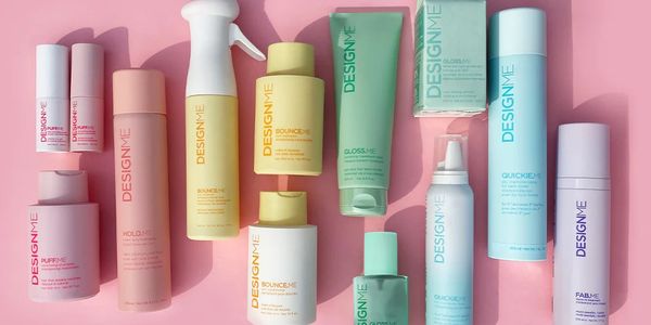 A collection of DESIGNME hair care products arranged neatly on a pink background.