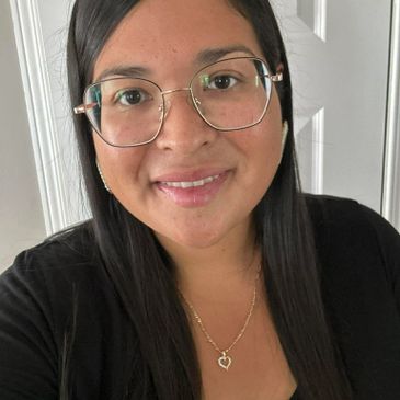 A woman with glasses and long black hair smiles gently at the camera.