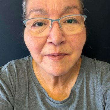 Close-up of a woman wearing glasses and a grey shirt against a dark background.