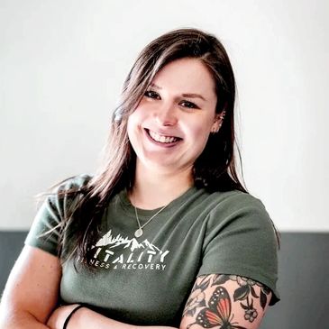 Smiling woman with tattoos and a green Vitality Fitness &amp; Recovery shirt.