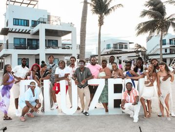 Group photo of friends posing by large white letters on a beach with palm trees.
