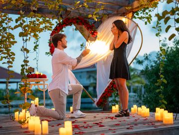 Man proposing to woman amid candlelit romantic setting outdoors.