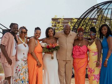 A group of seven people smiling, with a bride holding flowers in the center.