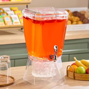 Clear beverage dispenser filled with orange drink and ice on a kitchen counter.