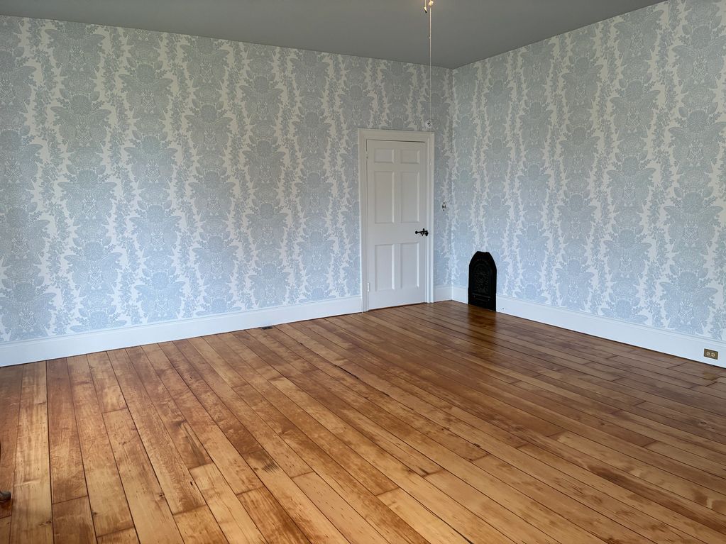 Empty room with wooden floors and patterned wallpaper.