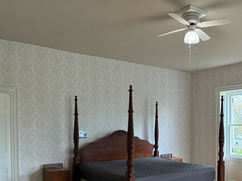 A vintage four-poster bed in a softly patterned bedroom with a ceiling fan.