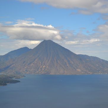 A mountain with a cloud hovering above it next to a large body of water.