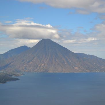 A mountain with a cloud hovering above it next to a large body of water.