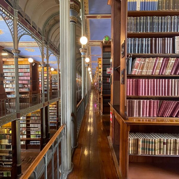 A long wooden corridor in an ornate library with tall bookshelves and decorative pillars.