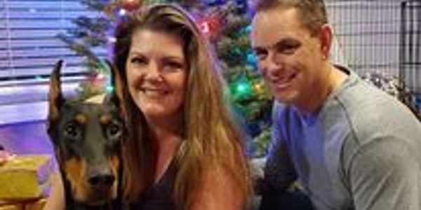 Couple with their Doberman dog by a Christmas tree.