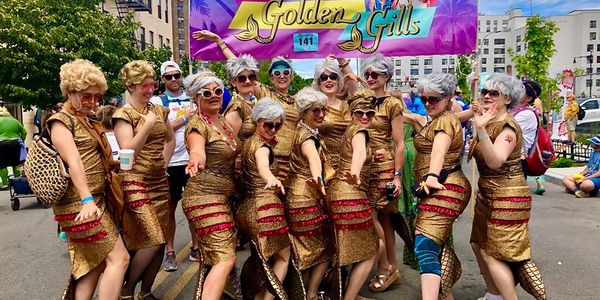 Group of people dressed in matching gold sequin outfits posing at an outdoor event.