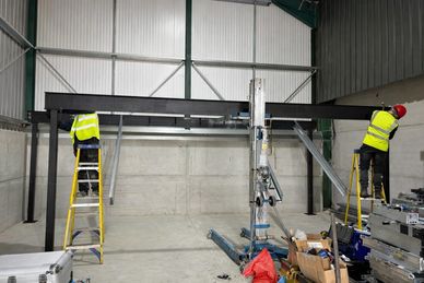 Two workers on ladders assembling a large metal frame inside a warehouse.