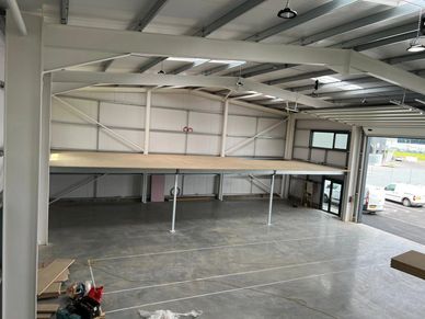 Empty industrial warehouse with a mezzanine floor and open garage door.