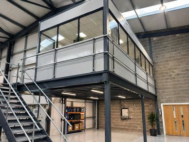 Modern industrial office mezzanine with glass walls and metal stairs.