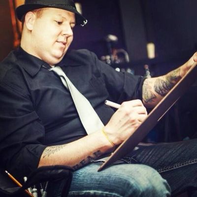 A man in a hat and tie sketches on a drawing board.