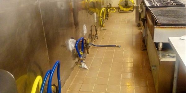 Industrial kitchen with gas valves and cooking equipment along a tiled floor.