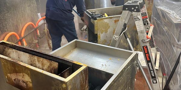 Industrial kitchen area with greasy equipment and a worker in the background.