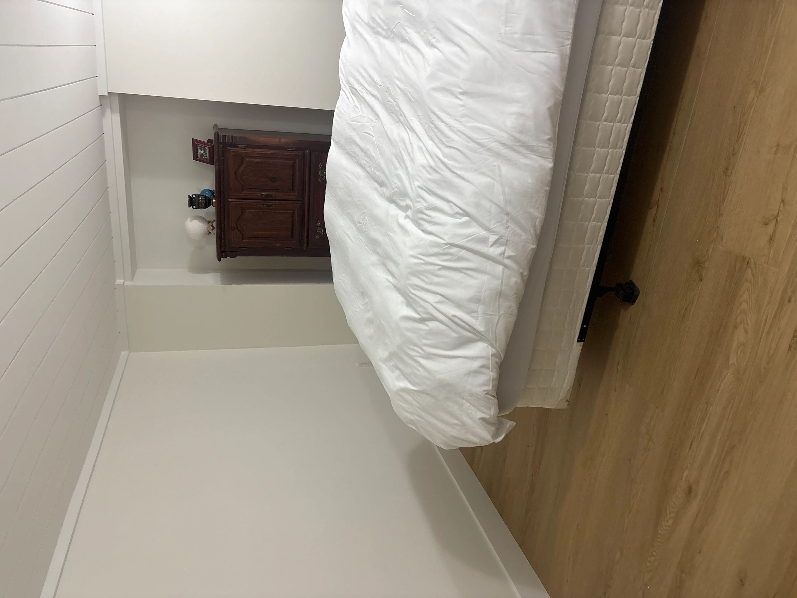 Minimalist bedroom with white bedding and wooden cabinet.