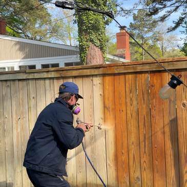 Man power washing a wooden fence on a sunny day.