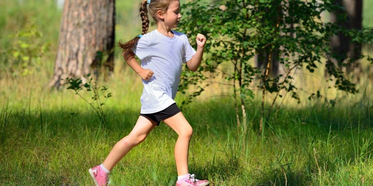 Young girl running energetically outdoors in a sunny forest.
